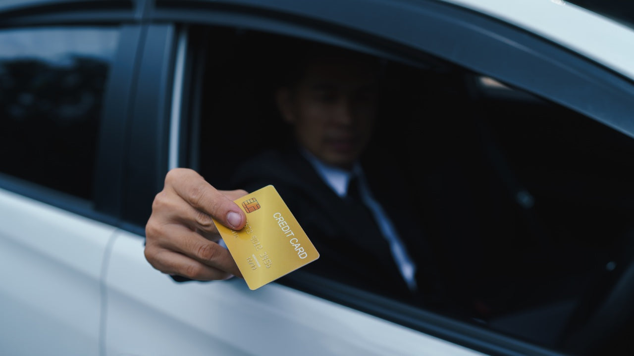 An image showing a colseup of a hand using a credit card to make payment for fuel  at a gas station.